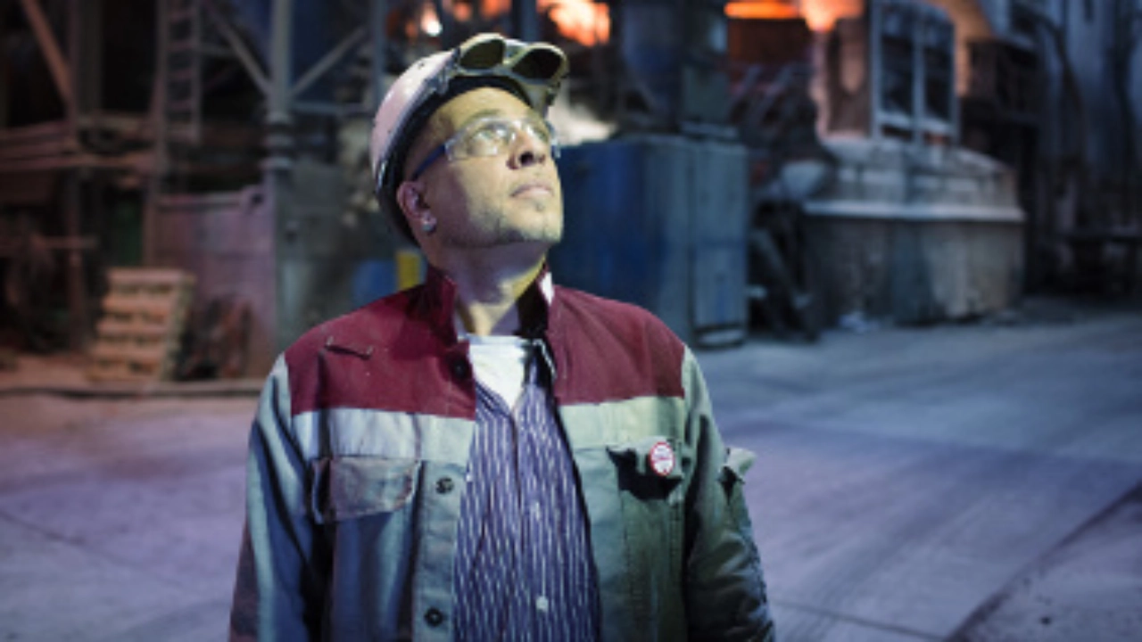 Ein Stahlarbeiter in Schutzkleidung mit Helm, der nach oben blickt.
