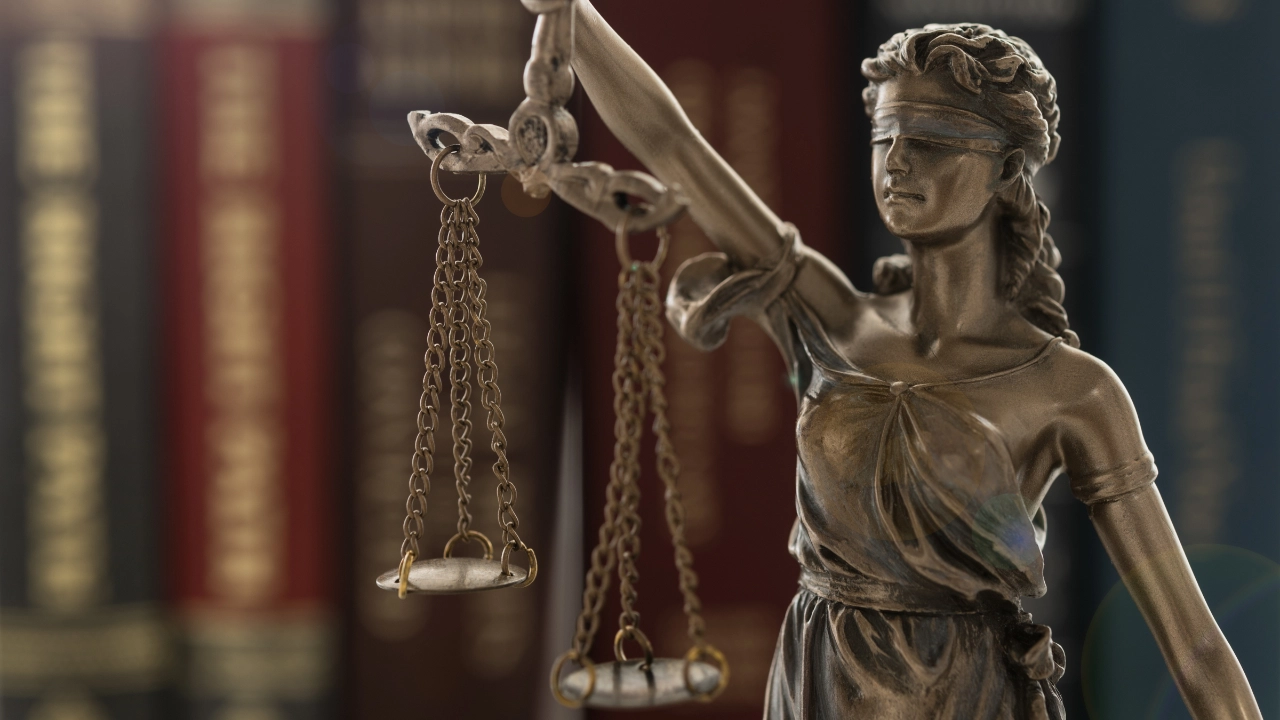 Bronzestatue von Justizia mit Waage in der Hand vor unscharfen Gesetzbüchern im Hintergrund