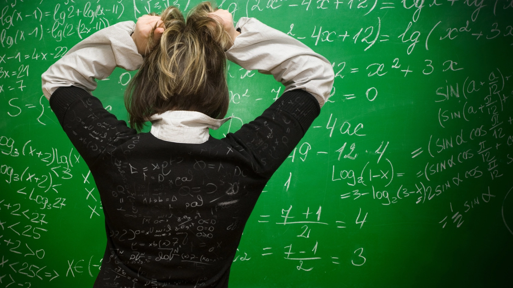 Frau steht vor einer Tafel mit vielen Formeln und rauft sich die Haare