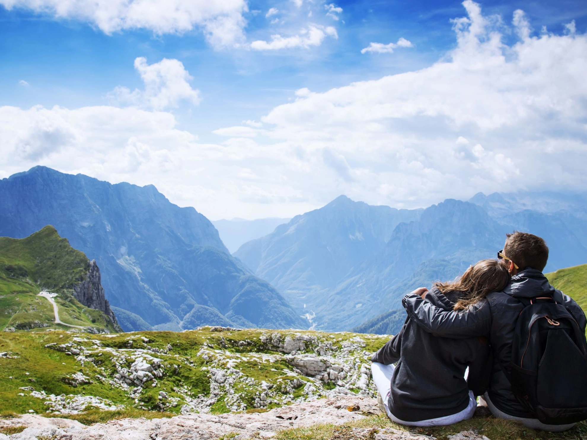 sitzendes Paar blickt von einem Berg auf ein Gebirge