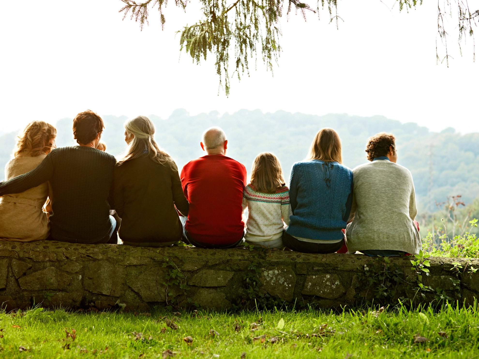 Mehrere Personen verschiedener Generationen sitzen auf einer Mauer.