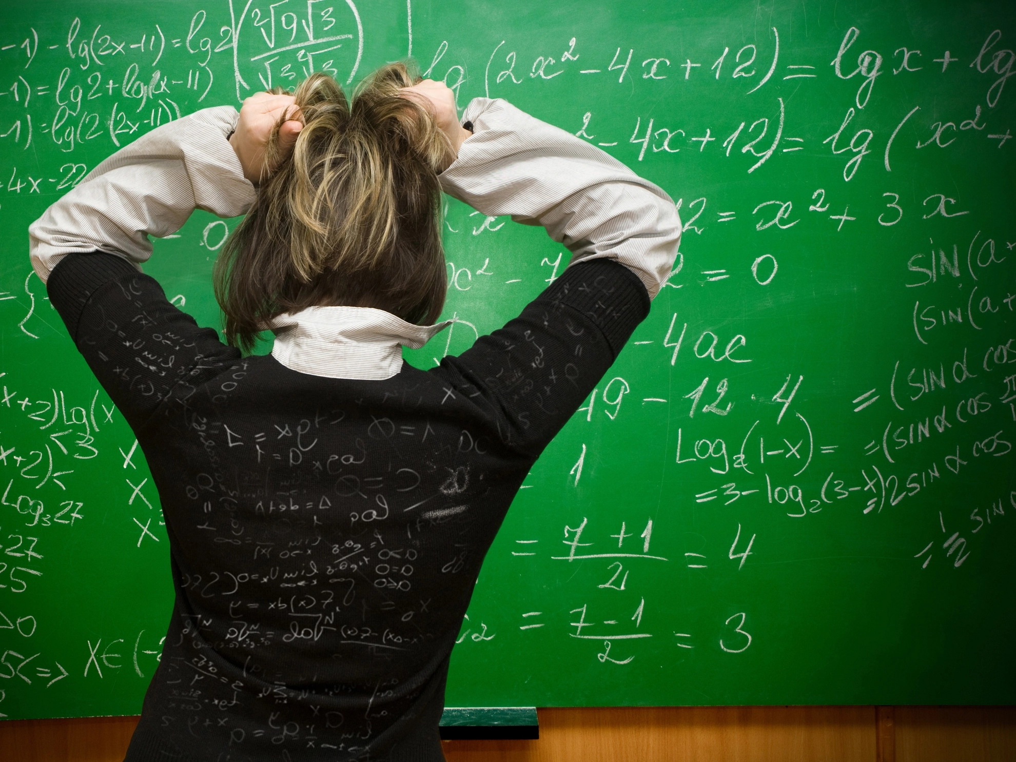 Frau steht vor einer Tafel mit vielen Formeln und rauft sich die Haare
