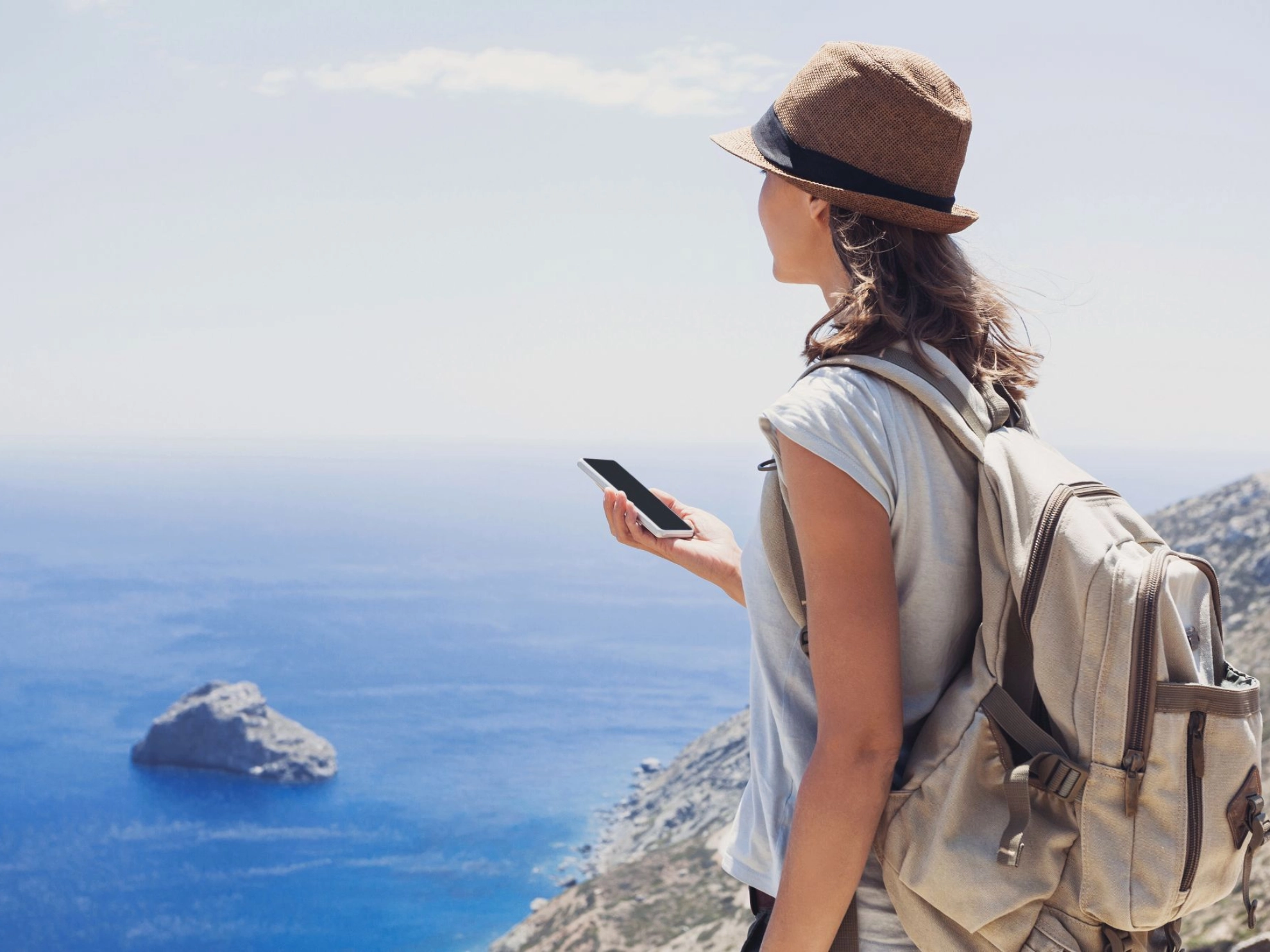 junge Frau beim Wandern am Meer, mit Smartphone und Rucksack